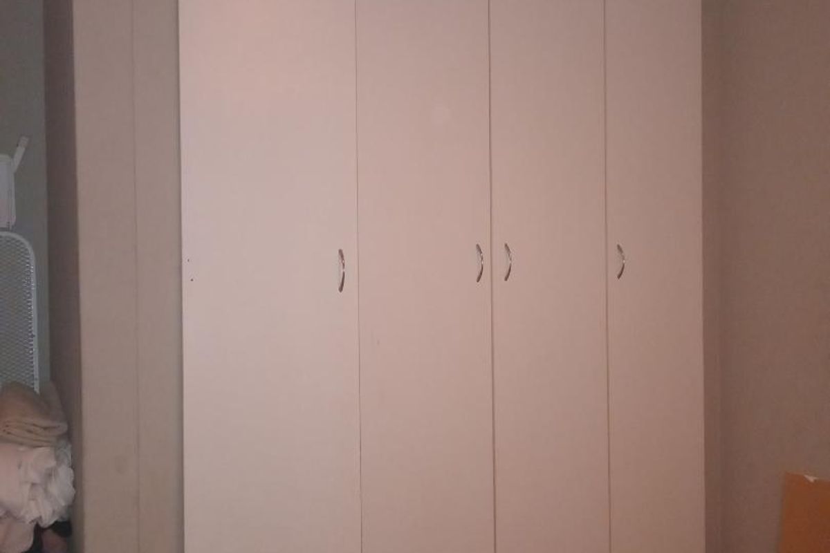 A bedroom featuring floor-to-ceiling built-in wardrobes with white cabinetry and tiled flooring.