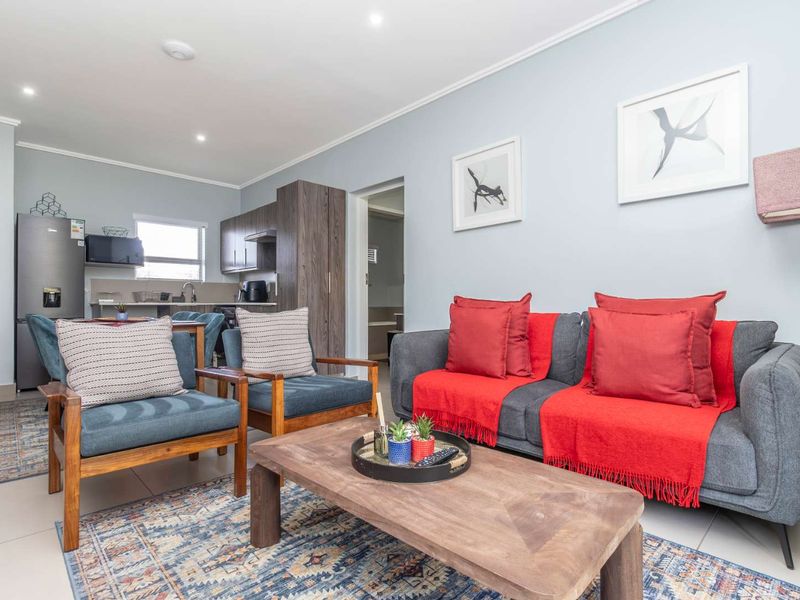 A bright open-plan living area featuring a modern kitchen with built-in cabinetry and tiled flooring, seamlessly connected to a comfortable lounge space.