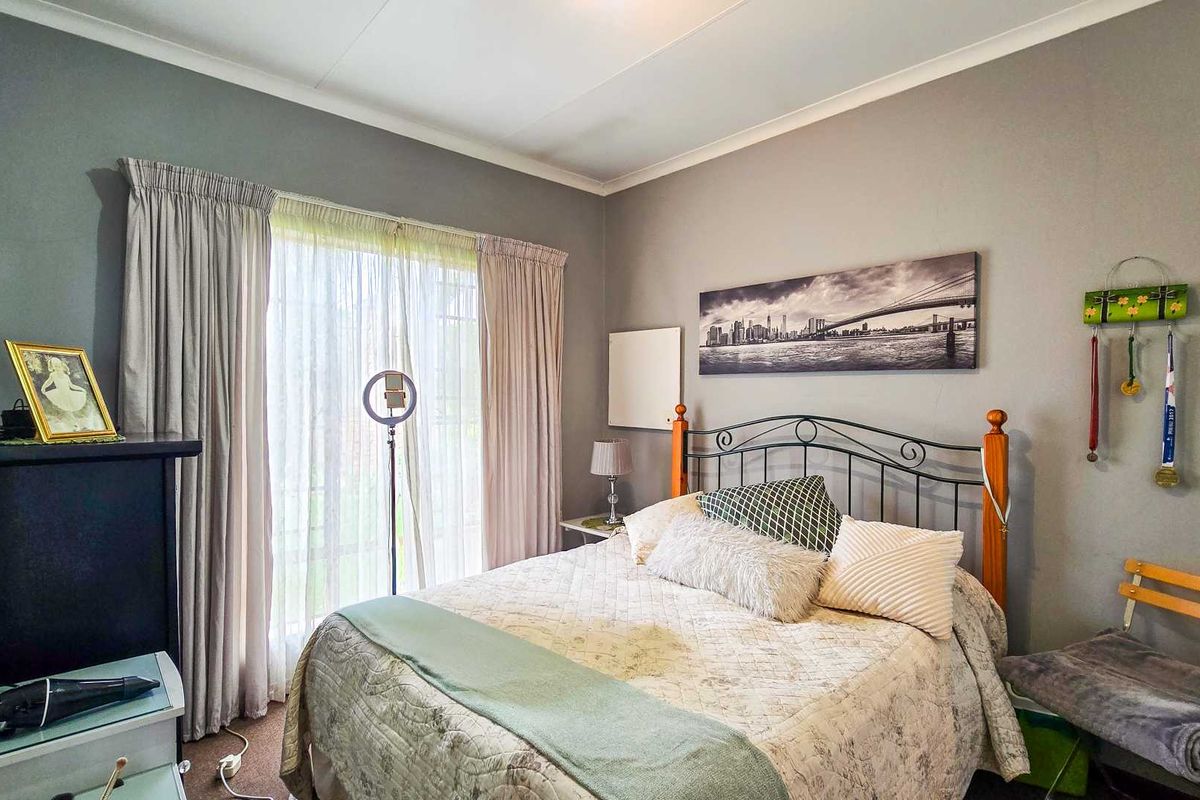A well-lit bedroom featuring neutral grey walls, a sliding glass door with curtains, and classic coving detail.