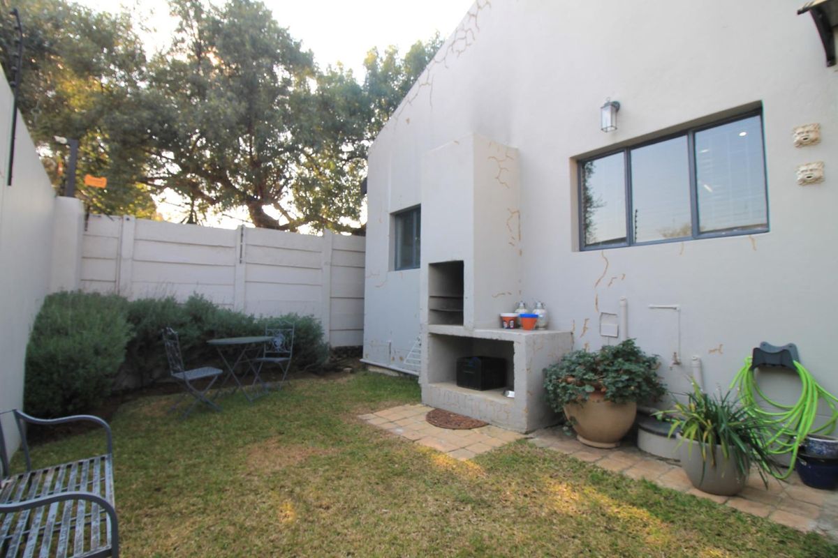 Rear garden area featuring a built-in braai, paved patio section, and precast concrete boundary walling.