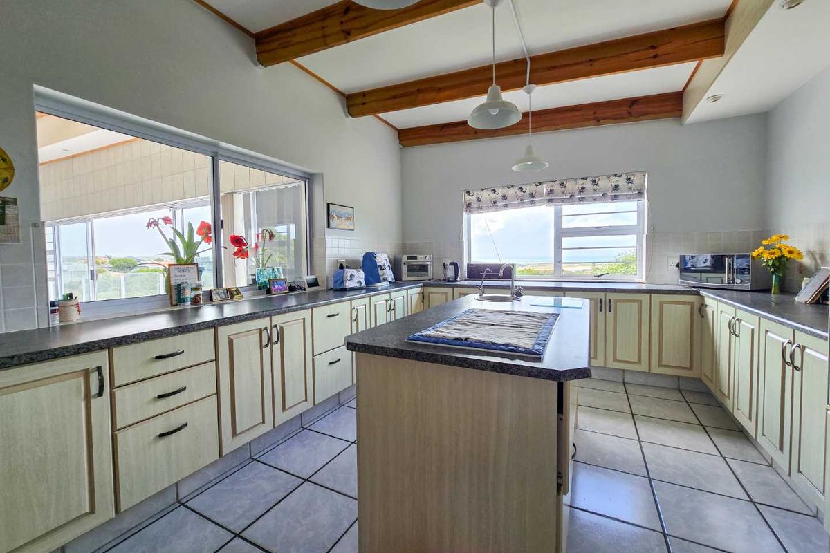 Spacious kitchen featuring a central island, ample cabinetry, tiled flooring, and exposed timber ceiling beams with large windows providing natural light.