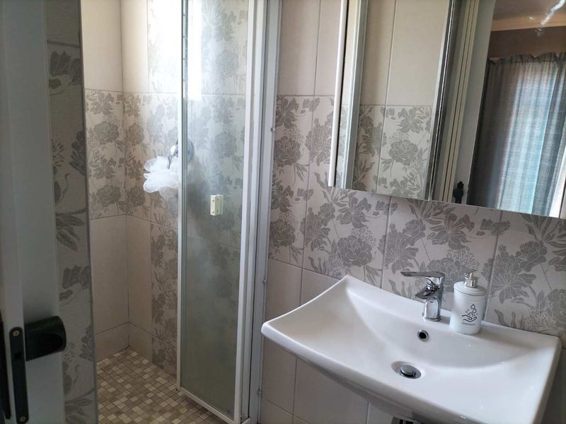 A functional bathroom featuring a shower enclosure, pedestal basin with chrome mixer tap, and decorative floral-patterned wall tiling.