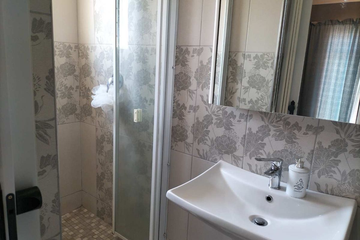 A functional bathroom featuring a shower enclosure, pedestal basin with chrome mixer tap, and decorative floral-patterned wall tiling.