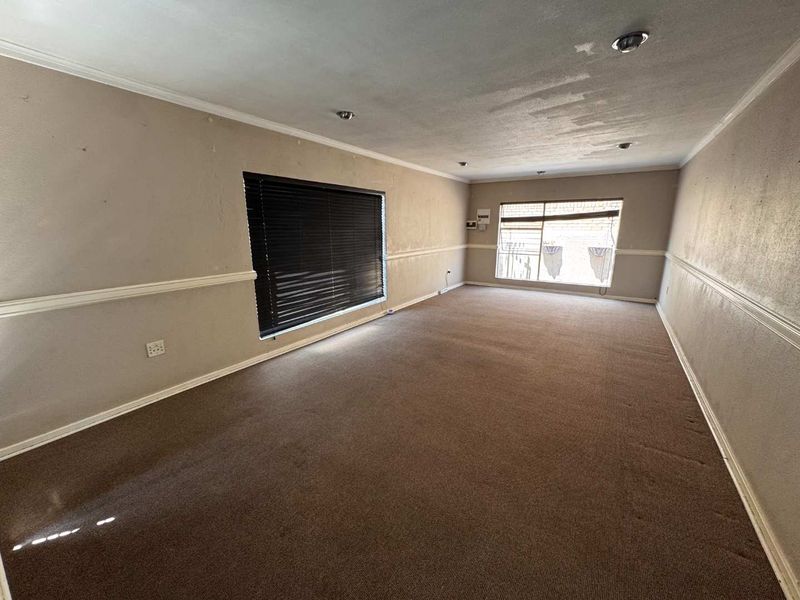 A spacious, empty living room featuring neutral walls with chair rail molding, recessed lighting, and carpet flooring, ready for a fresh update.