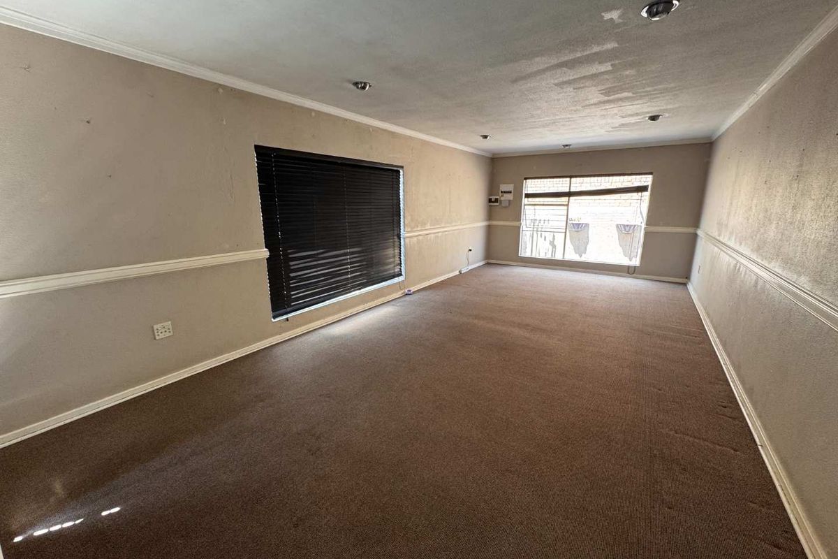 A spacious, empty living room featuring neutral walls with chair rail molding, recessed lighting, and carpet flooring, ready for a fresh update.