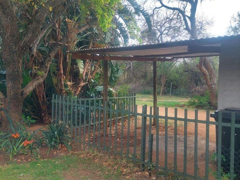 A rear outdoor area featuring a simple corrugated iron roof structure supported by timber posts, enclosed by a metal picket fence.