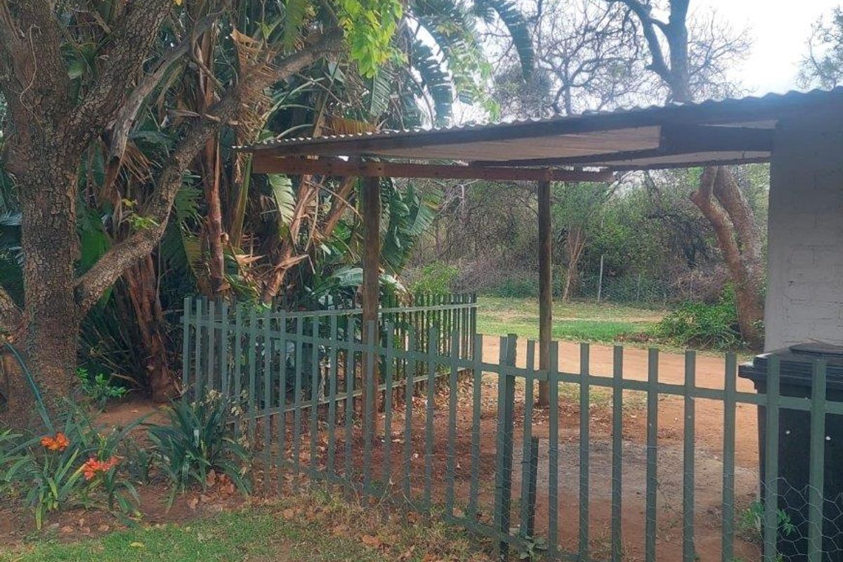 A rear outdoor area featuring a simple corrugated iron roof structure supported by timber posts, enclosed by a metal picket fence.