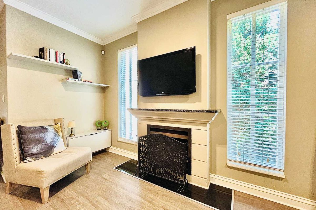 A cozy living room featuring a central fireplace with a mantel, built-in shelving, and large windows with fitted blinds.