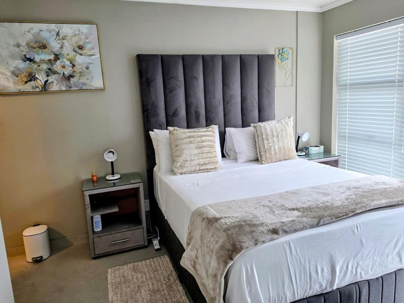 A well-maintained bedroom featuring neutral wall tones, a tall upholstered headboard, and venetian blinds for adjustable natural light.