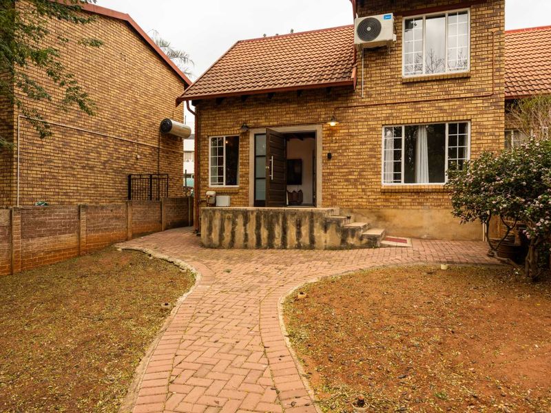 Rear view of a brick townhouse featuring a paved patio area, garden walkway, and exterior wall-mounted air conditioning unit.