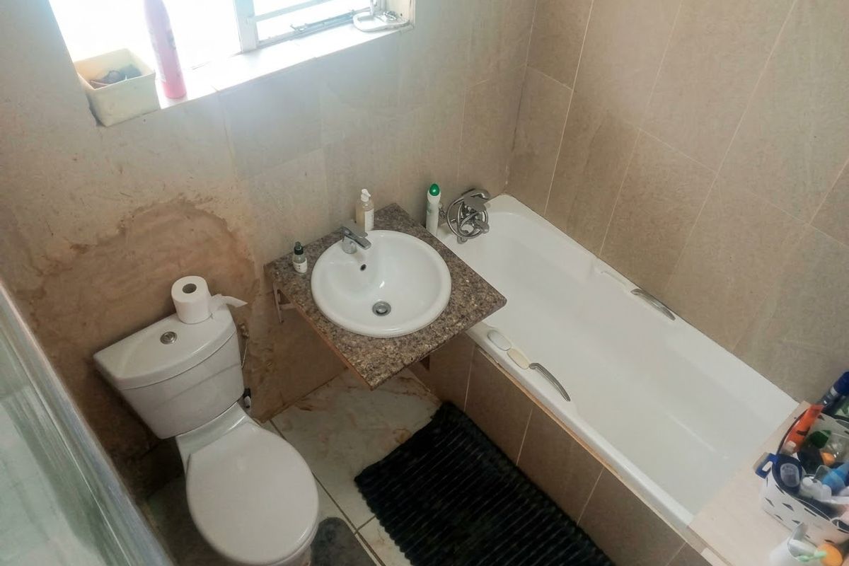 Compact bathroom featuring a built-in bathtub, wall-mounted vanity basin, and toilet with neutral wall tiling. Requires cosmetic attention to wall finishes.