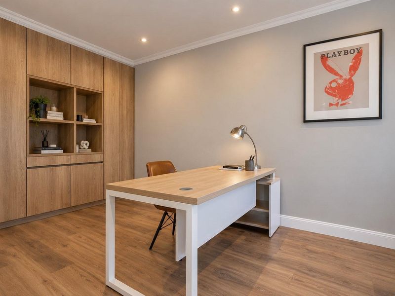A modern home office featuring custom built-in timber cabinetry, recessed downlighting, and high-quality laminate flooring in a neutral, well-maintained space.
