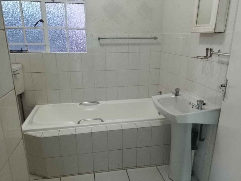 A dated bathroom featuring a pedestal basin, built-in bathtub, and tiled finishes, offering a blank canvas for renovation and modernization.