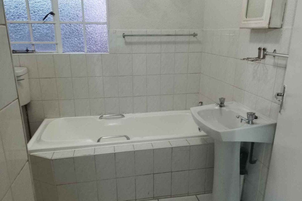 A dated bathroom featuring a pedestal basin, built-in bathtub, and tiled finishes, offering a blank canvas for renovation and modernization.
