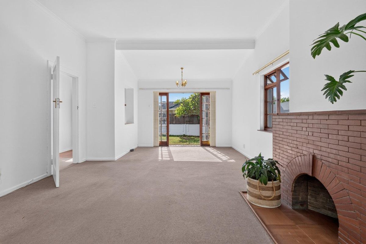 Spacious living room featuring a classic brick fireplace, neutral carpeting, and timber-framed french doors providing direct access to the rear garden.