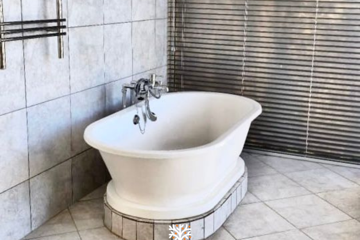 A bathroom featuring a freestanding bathtub with chrome fixtures, tiled flooring, wall tiling, and horizontal window blinds.