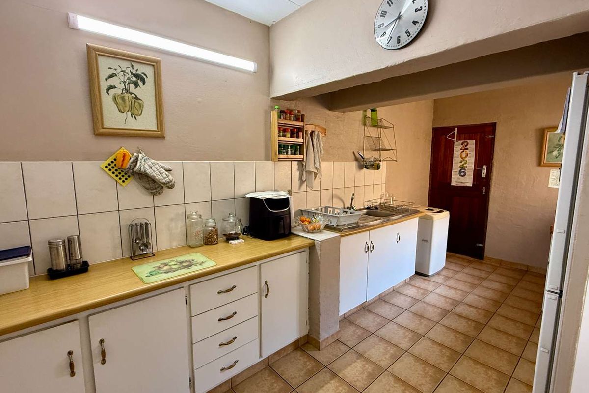 A functional kitchen featuring laminate countertops, white cabinetry, tiled backsplash, and floor tiles, providing a practical workspace with integrated sink and utility area.