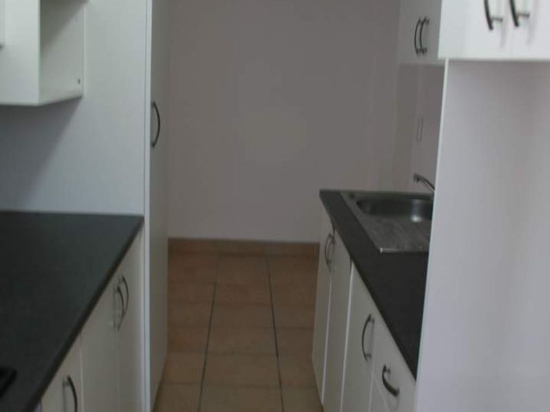 A compact, functional kitchen featuring white cabinetry, dark countertops, and tiled flooring, offering a clean and neutral space ready for personalization.