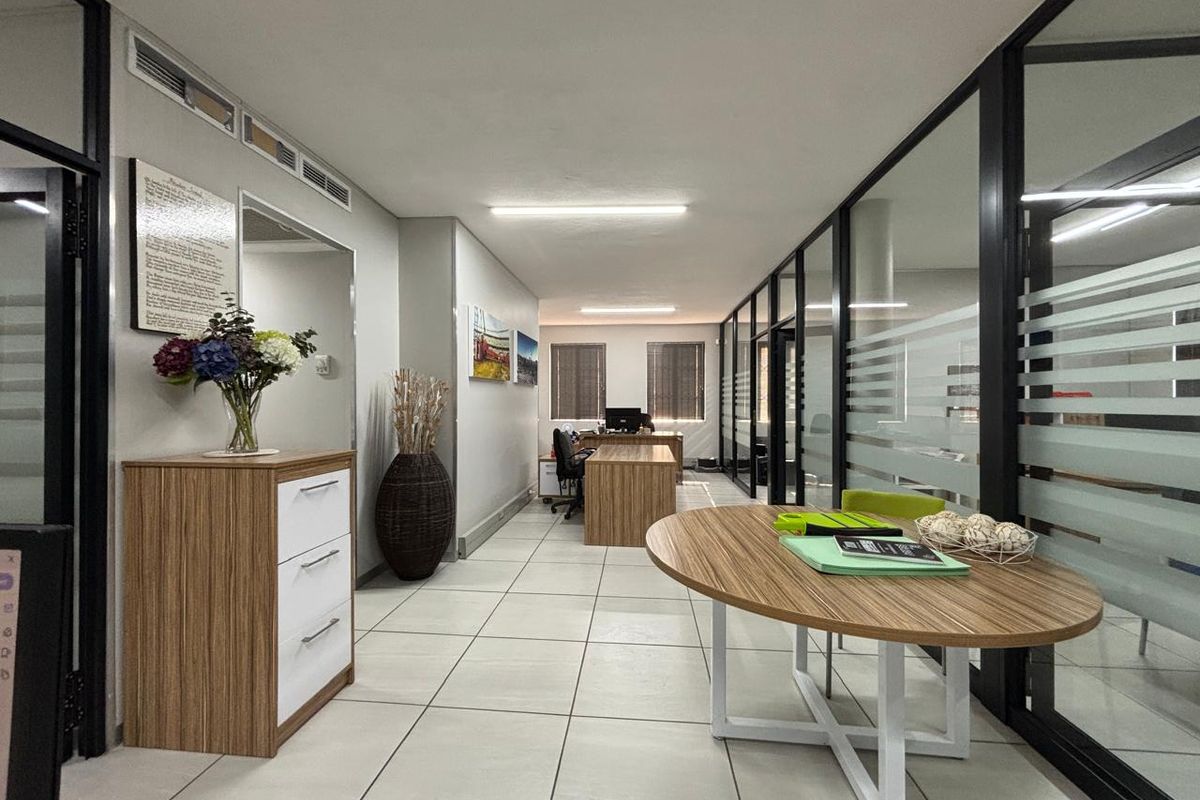 A modern office space featuring glass partition walls, tiled flooring, and integrated air conditioning, providing a professional and well-lit work environment.