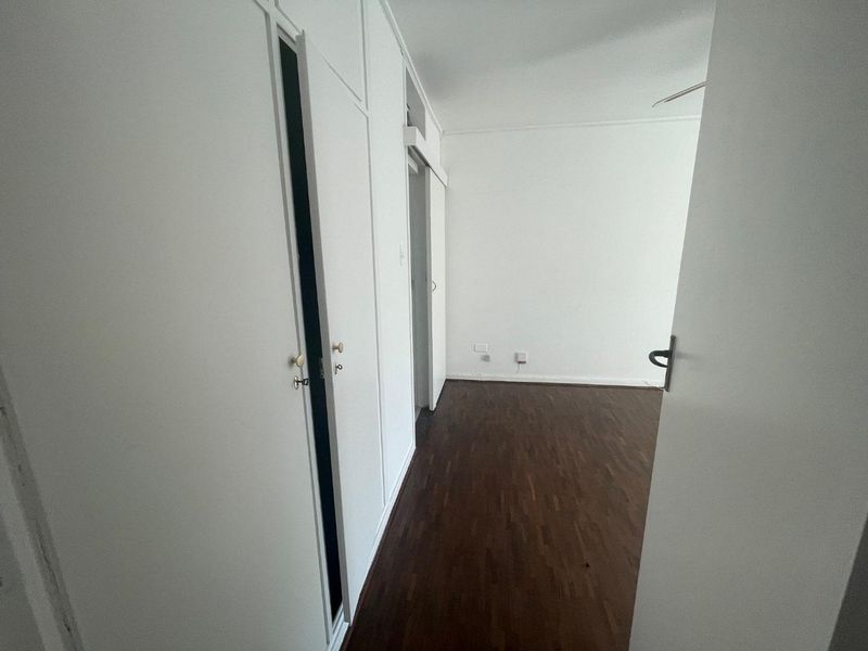 An empty bedroom featuring dark parquet flooring and extensive built-in cupboard storage with white cabinetry.
