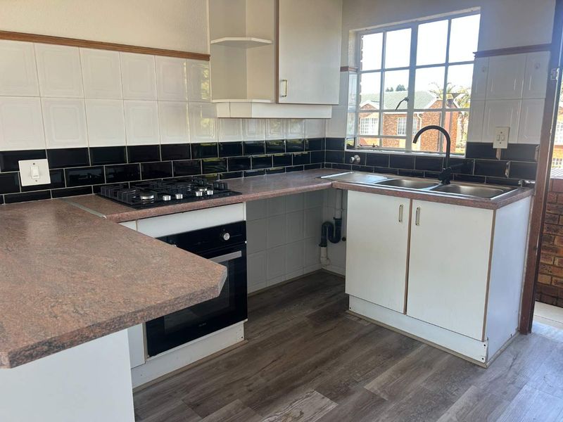 A functional kitchen featuring a gas hob, built-in oven, double sink, and tiled backsplash with ample laminate countertop space.