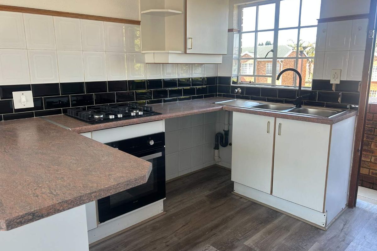 A functional kitchen featuring a gas hob, built-in oven, double sink, and tiled backsplash with ample laminate countertop space.