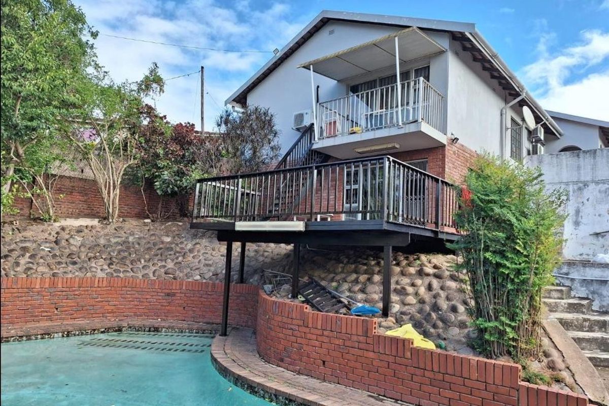 Rear exterior view featuring a swimming pool, raised timber deck, balcony, and external staircase set against a brick retaining wall.
