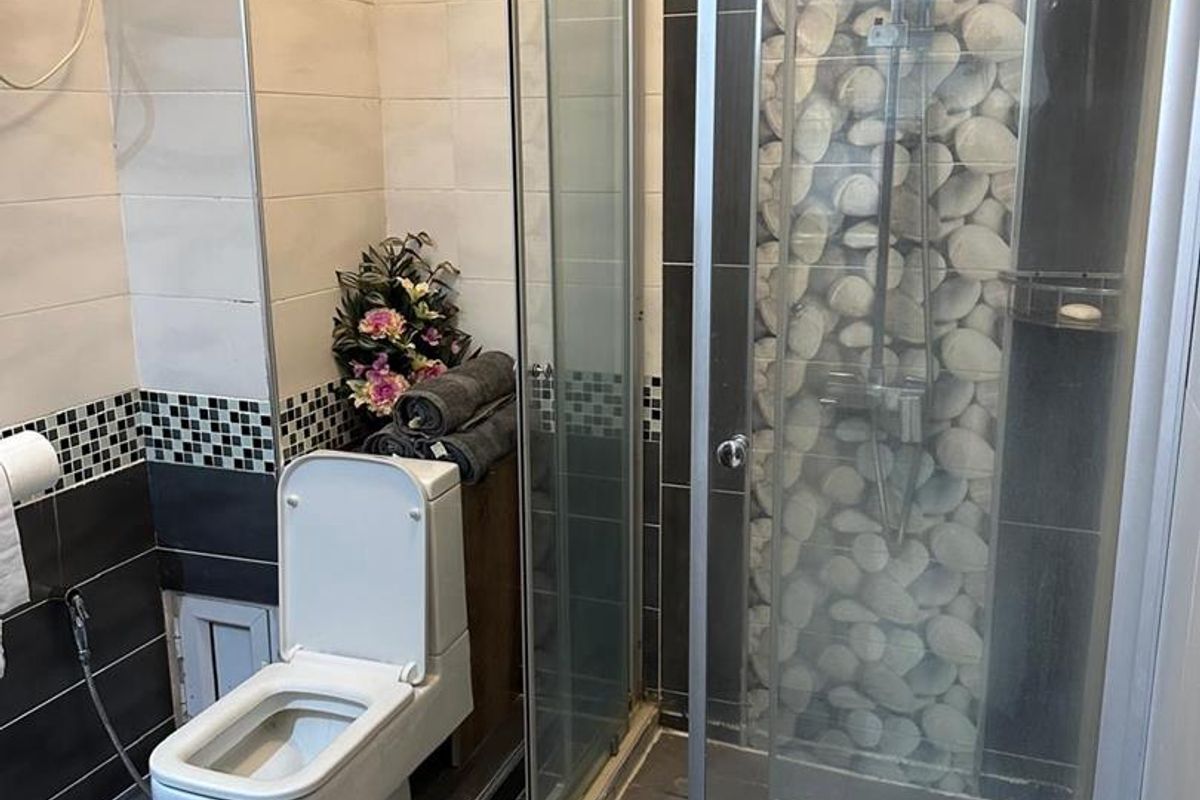 A functional bathroom featuring a glass-enclosed shower with decorative stone-effect tiling, a modern toilet, and wall-mounted water heater.