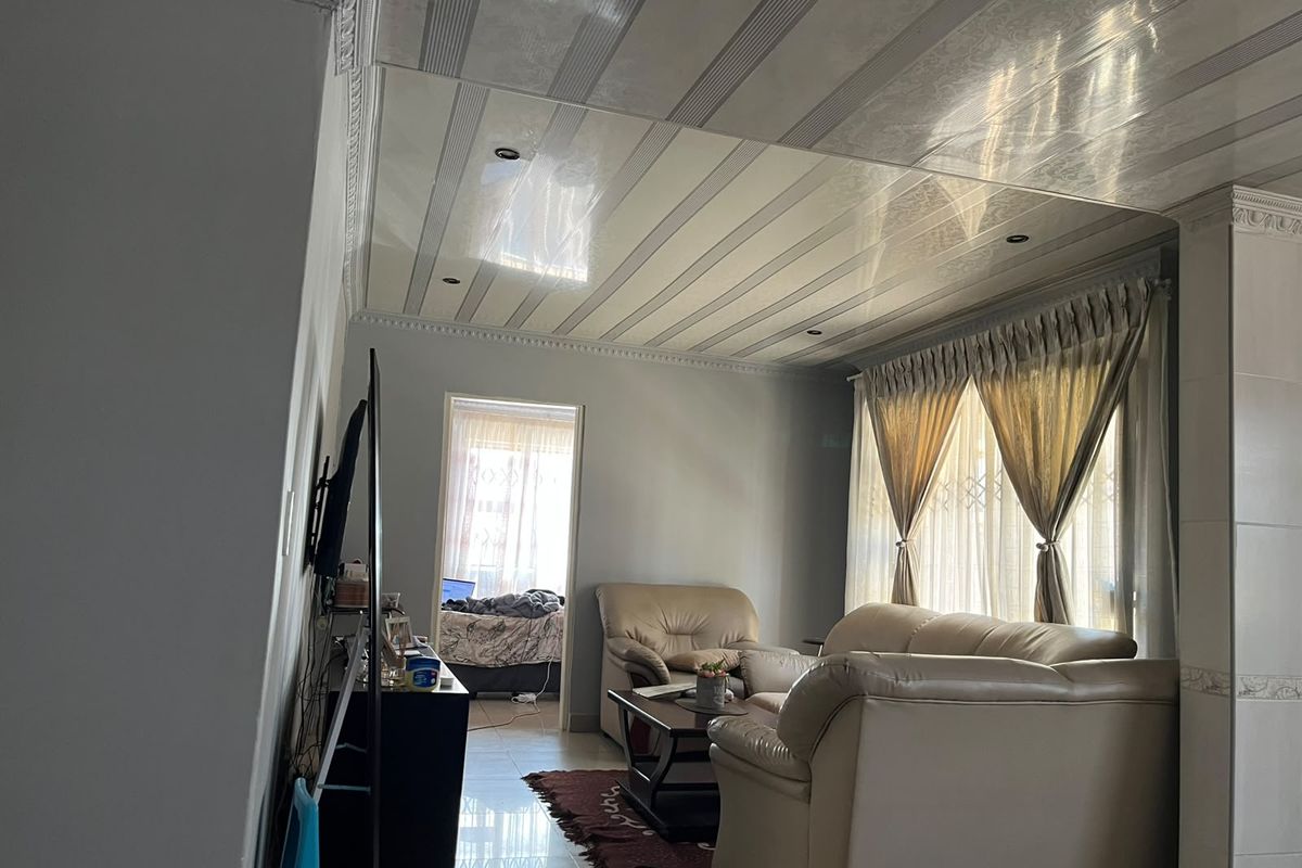 A living room featuring tiled flooring, decorative ceiling panels with recessed downlights, and crown molding, providing a functional and well-lit living space.