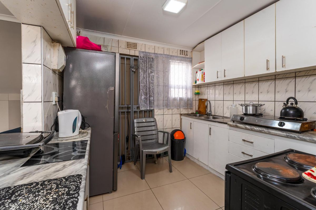 A compact kitchen featuring white cabinetry, tiled walls, and a stainless steel sink, requiring cosmetic updates to modernize the space.