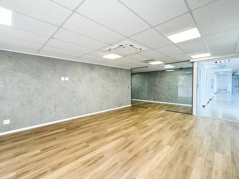 Modern, open-plan office space featuring high-quality laminate flooring, a textured feature wall, glass partitioning, and integrated cassette air conditioning.