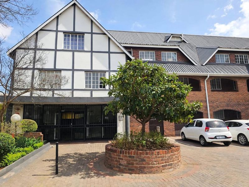 Front elevation of a Tudor-style apartment complex featuring brick paving, a central brick planter, and secure gated entrance.