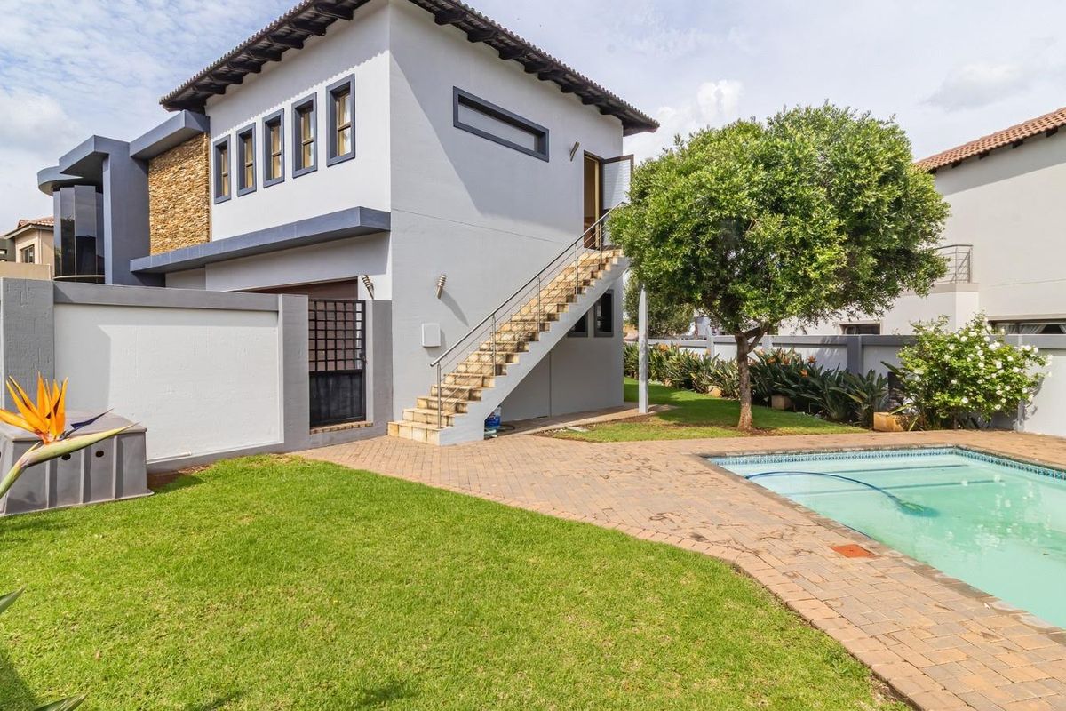 Rear view of the property featuring a swimming pool, paved patio area, landscaped garden, and an external staircase leading to the upper level.