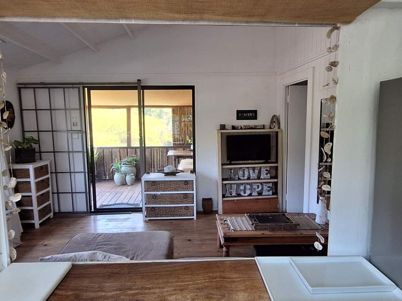 Open plan living area featuring timber flooring, exposed beam ceilings, and direct access to an outdoor timber deck through sliding glass doors.