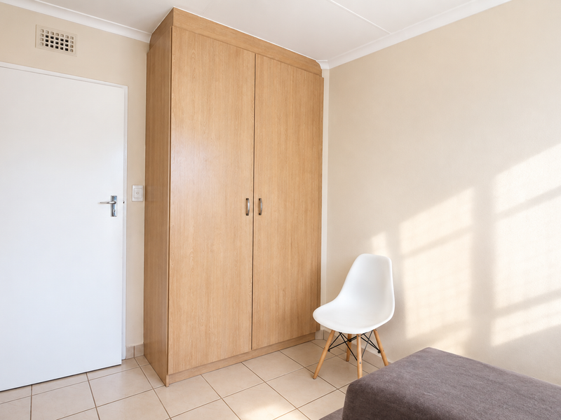 A bright bedroom featuring neutral walls, tiled flooring, and a functional built-in wooden wardrobe.