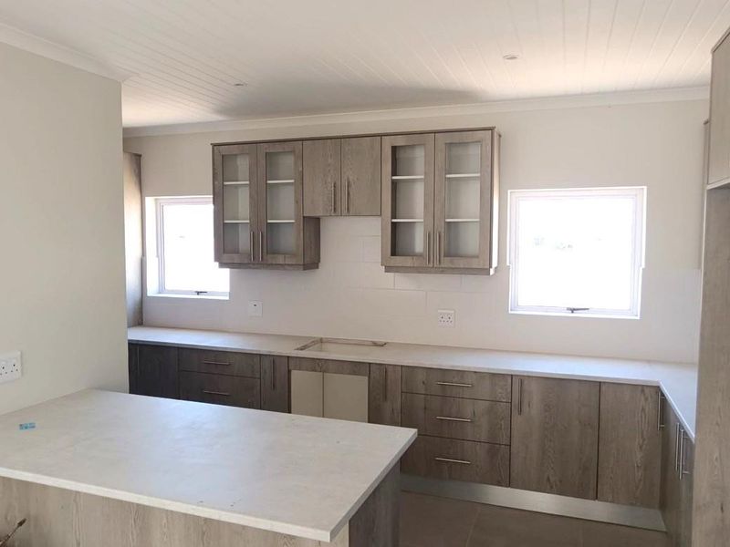 A modern, empty kitchen featuring wood-grain cabinetry, stone countertops, and a tongue and groove ceiling, awaiting final appliance installation and finishing touches.