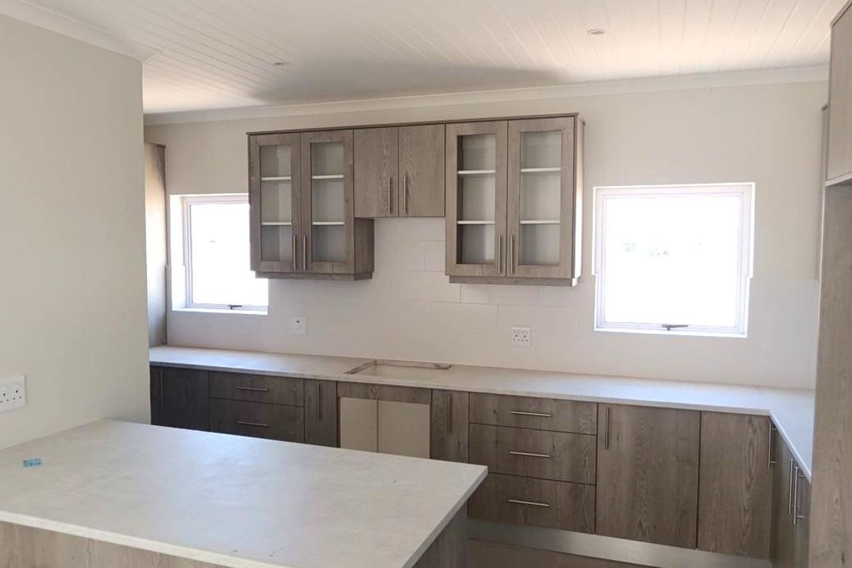A modern, empty kitchen featuring wood-grain cabinetry, stone countertops, and a tongue and groove ceiling, awaiting final appliance installation and finishing touches.