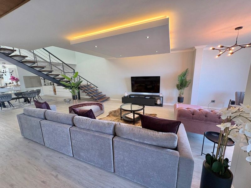 Spacious open-plan living area featuring a modern floating staircase, recessed ceiling with ambient lighting, and high-quality laminate flooring.