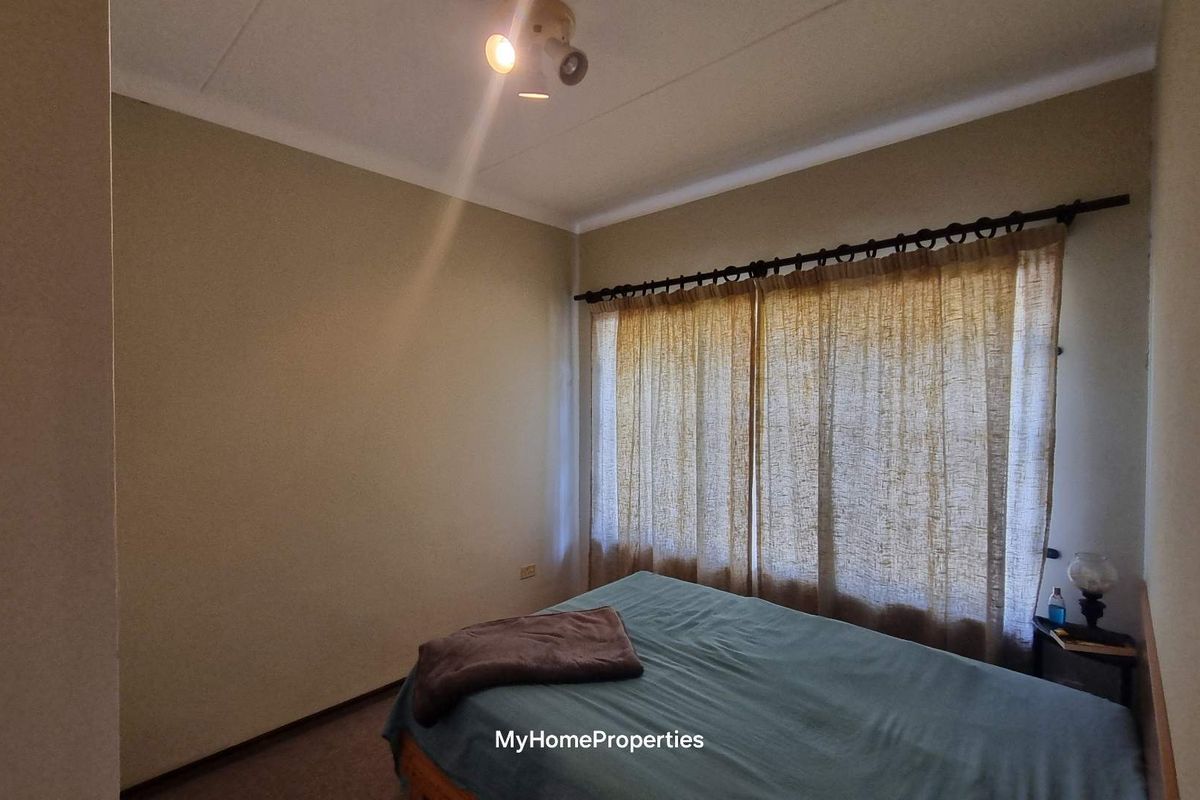 A bedroom featuring neutral wall tones, carpeted flooring, and a window dressed with curtains.