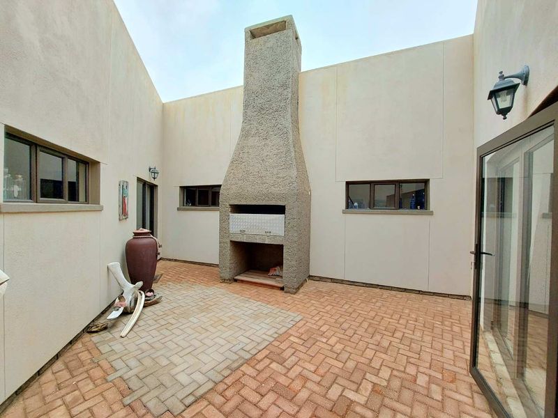 An enclosed outdoor patio area featuring a built-in braai, brick paving, and direct access to the interior through a sliding door.