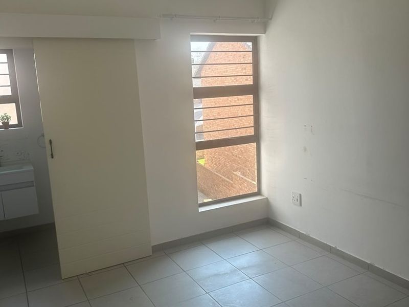 An empty bedroom featuring tiled flooring, a sliding door, and a window with security bars, offering a clean and neutral space.