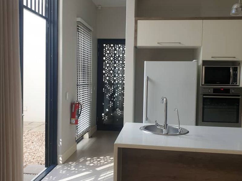 Modern kitchen featuring a central island with sink, built-in oven and microwave, tiled flooring, and direct access to an outdoor area through sliding doors.
