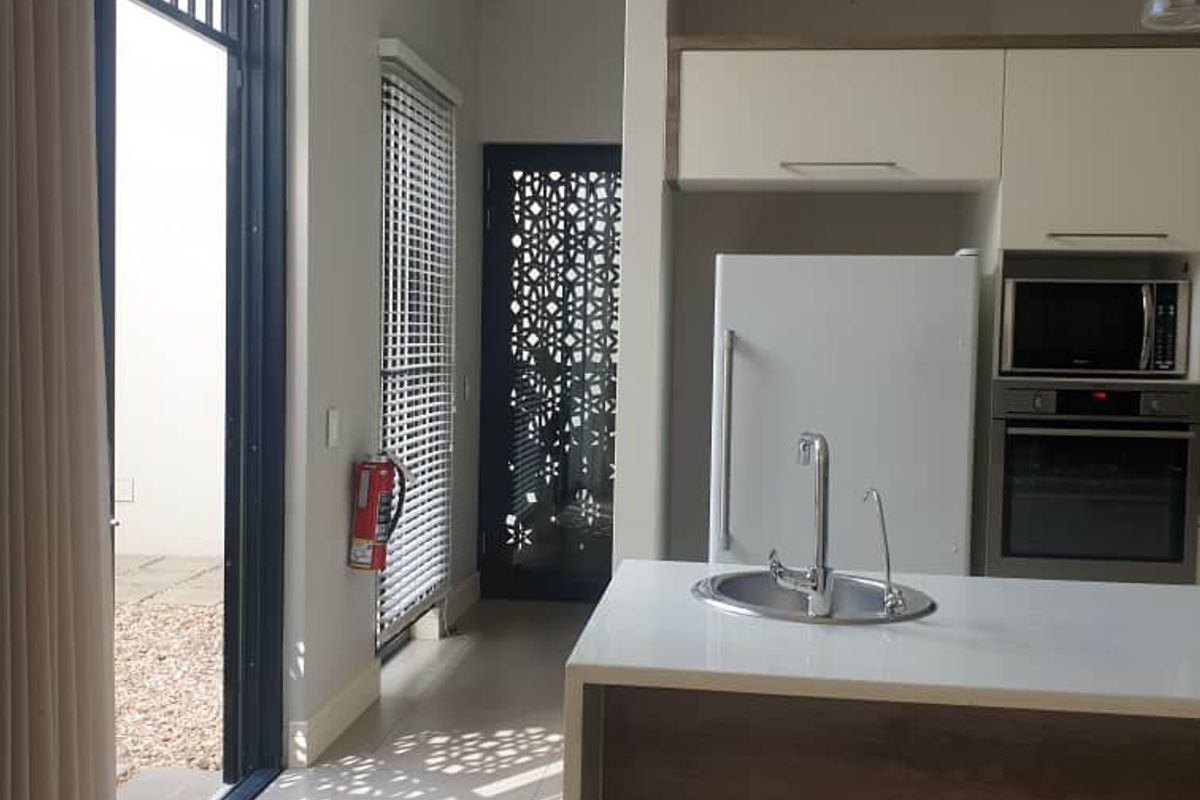 Modern kitchen featuring a central island with sink, built-in oven and microwave, tiled flooring, and direct access to an outdoor area through sliding doors.