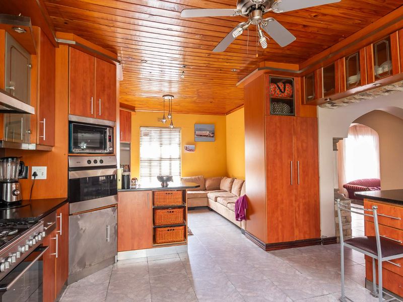 Open-plan kitchen and living area featuring timber ceilings, built-in cabinetry, integrated appliances, and tiled flooring with an arched transition to adjacent space.
