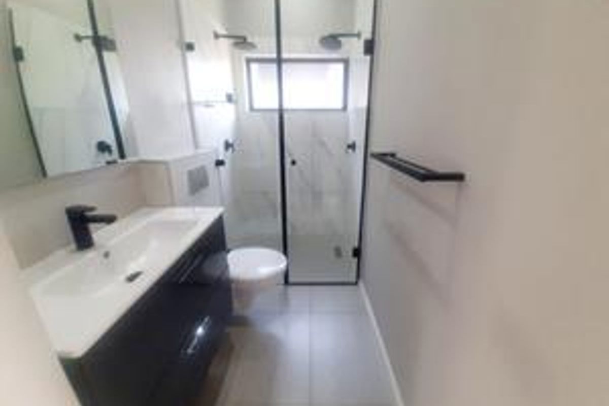Modern bathroom featuring a sleek vanity, wall-hung toilet, and a spacious walk-in shower with contemporary black fixtures and neutral tiling.