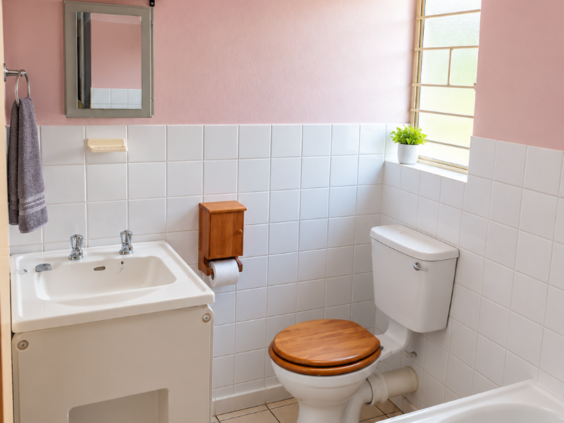 A functional bathroom featuring a pedestal washbasin, toilet, and bathtub with white wall tiling and neutral floor tiles.
