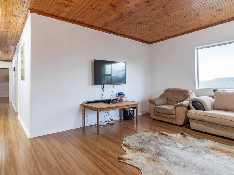 A living room featuring a distinctive timber-clad ceiling, laminate flooring, and a large window providing natural light.