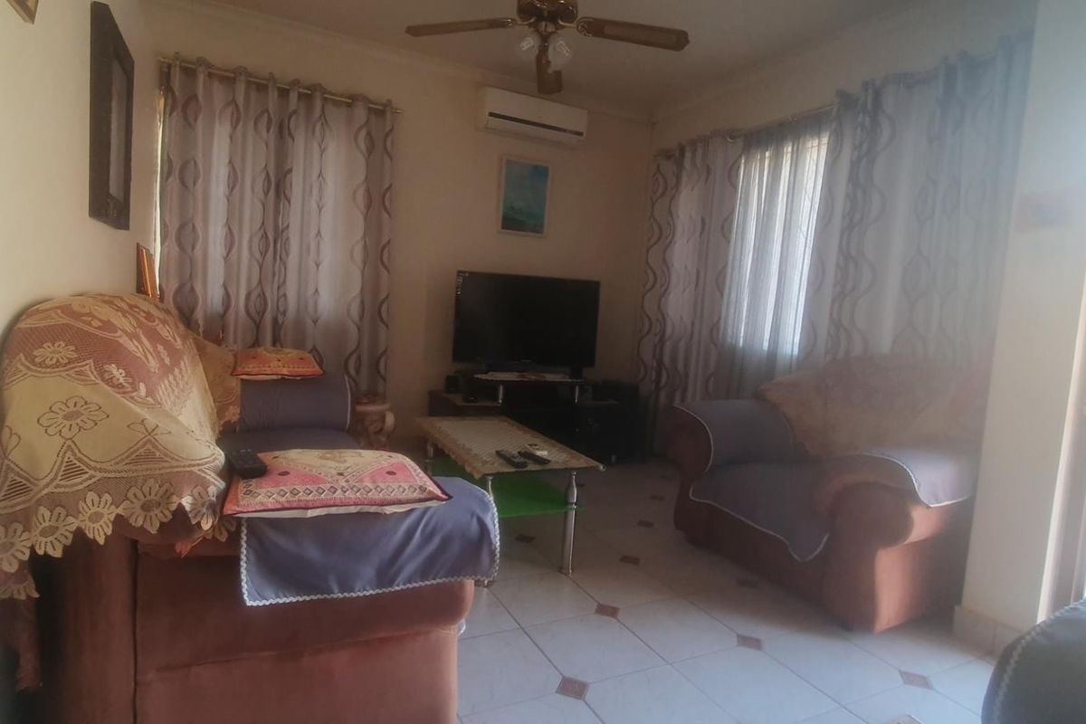A functional living room featuring tiled flooring, a ceiling fan, and a wall-mounted split-system air conditioner.