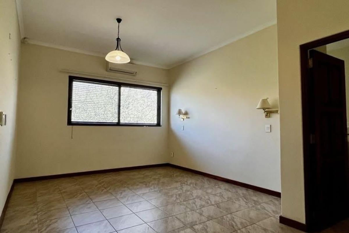 A spacious, empty bedroom featuring tiled flooring, a split-system air conditioner, and wall-mounted lighting, providing a neutral canvas for personalization.