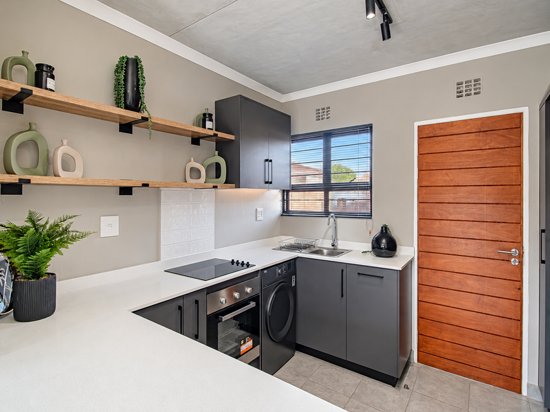 Modern kitchen featuring charcoal cabinetry, stone countertops, built-in oven, electric hob, and floating timber shelving with a sleek, contemporary finish.